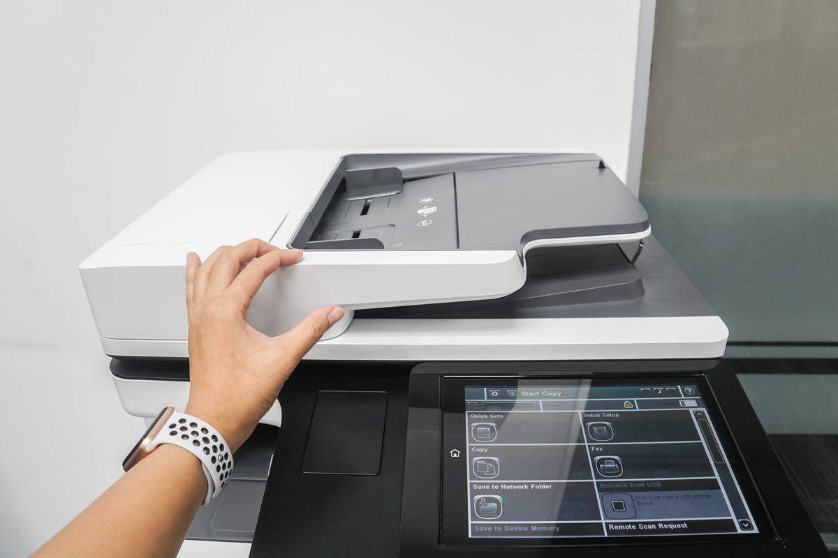 A person operates a modern printer, lifting its lid. The touchscreen displays various options, conveying efficiency and technology.