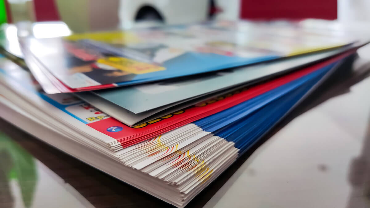 A stack of colorful magazines fanned out on a reflective surface, with vivid reds, blues, and yellow covers.