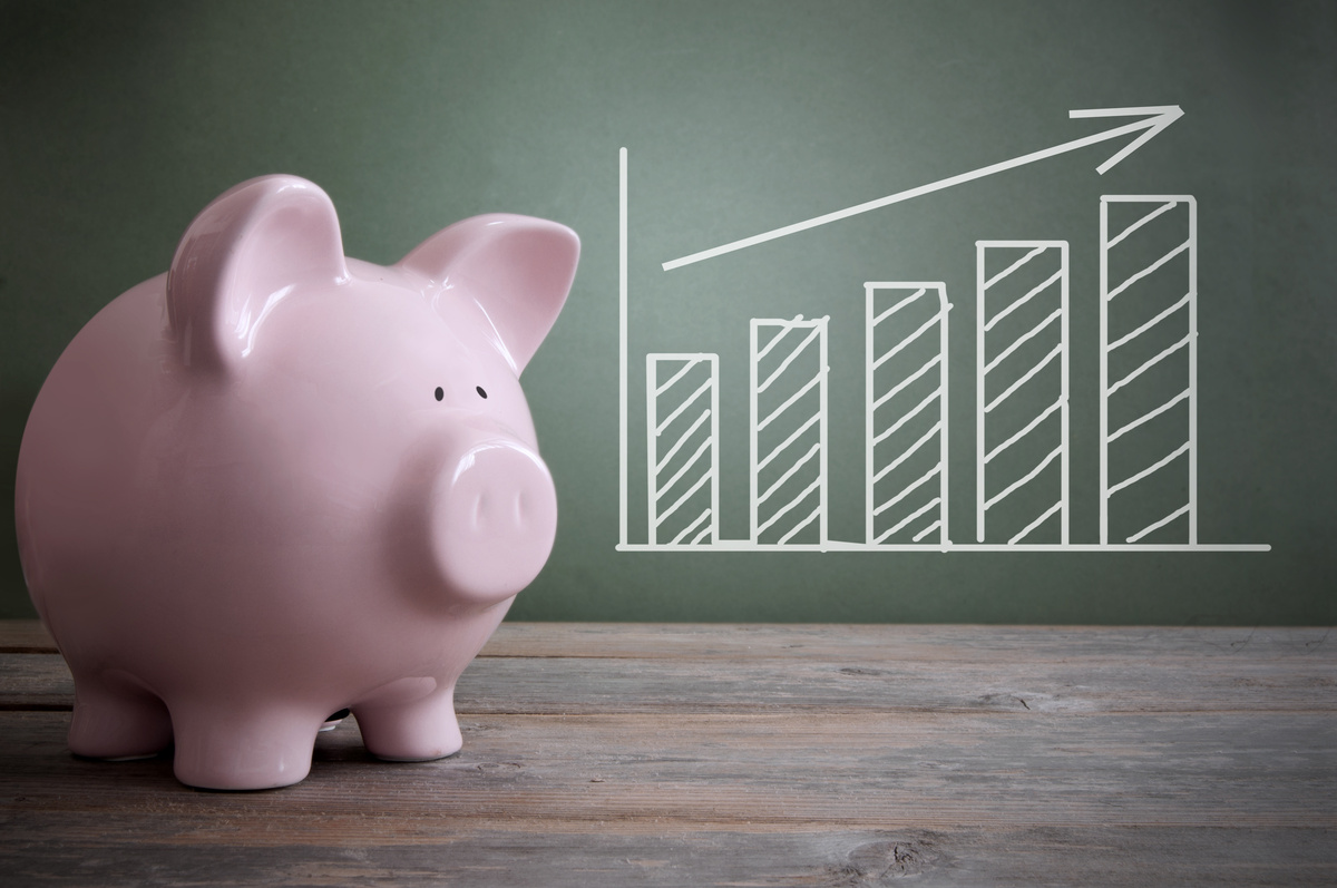 A pink piggy bank sits on a wooden surface against a green background with a chalk-drawn ascending bar graph, symbolizing financial growth and savings.