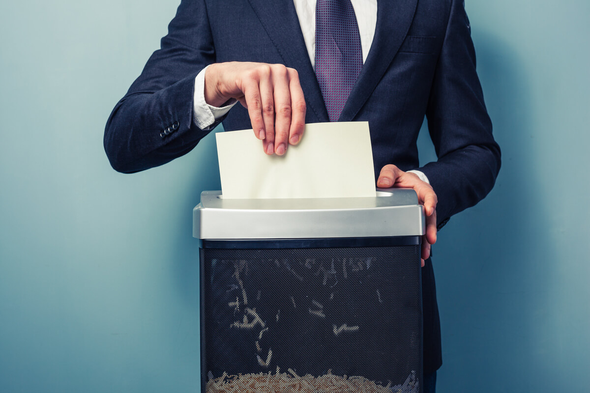 A person in a suit shreds a paper in an office shredder. 