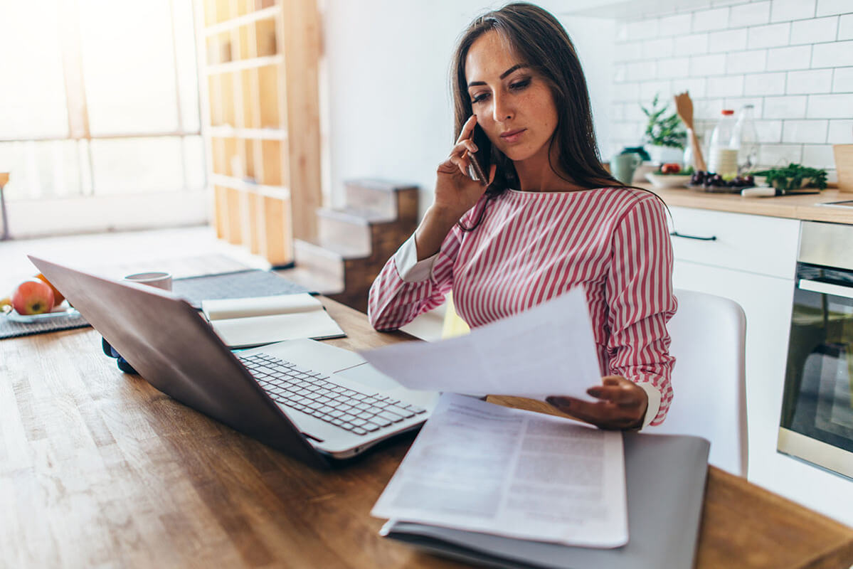 Woman on phone and laptop looking over paperwork