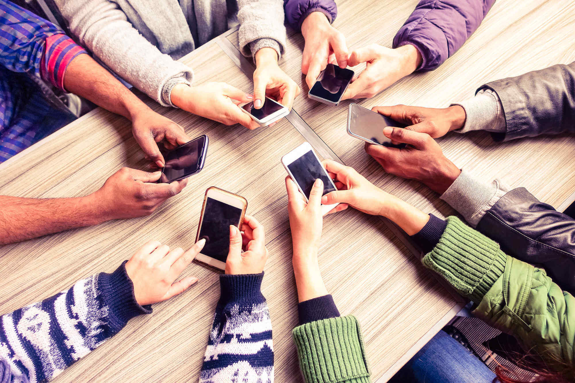 Top view of group sitting in a circle at a desk all using their mobile phones