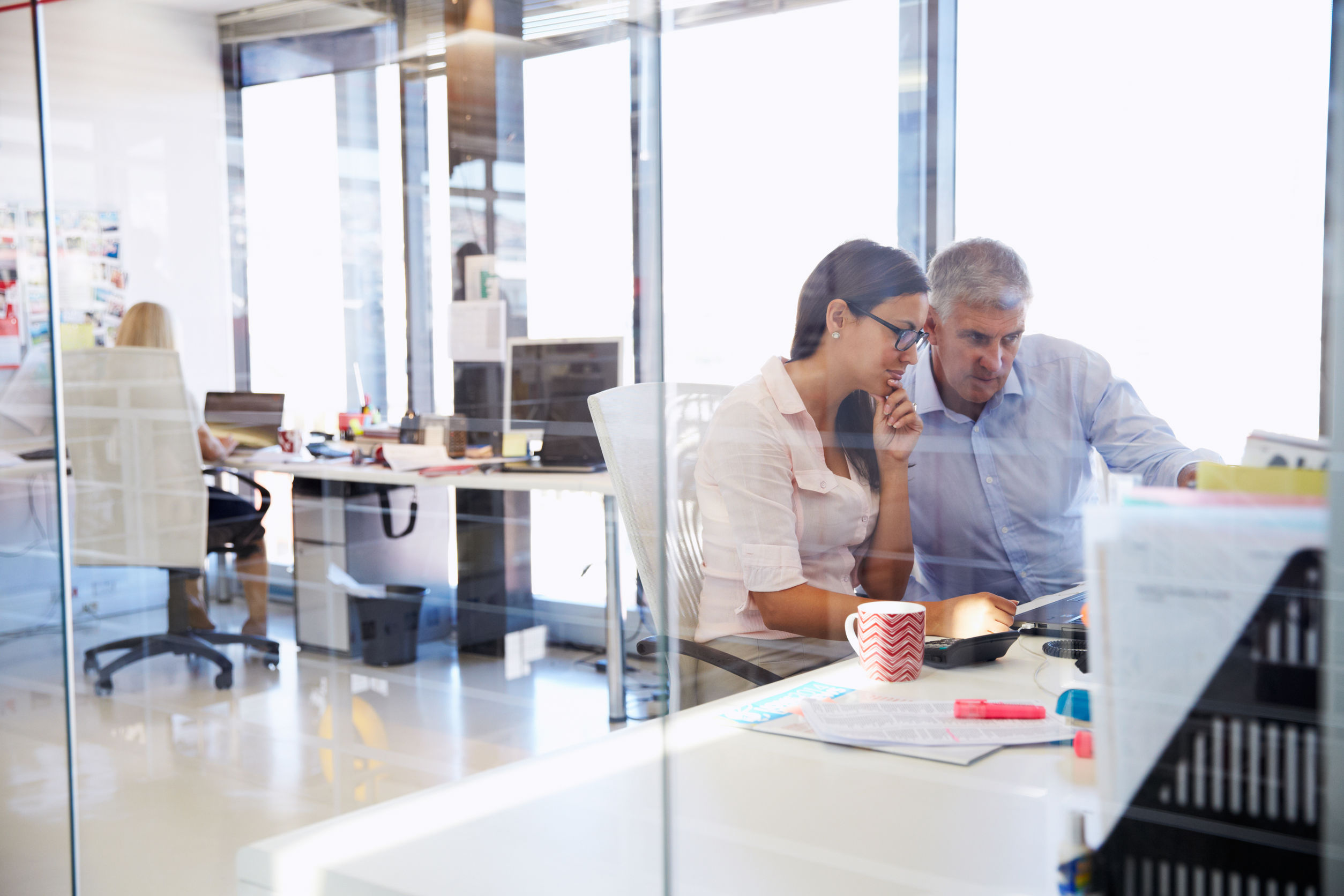 Two business professionals collaborating on laptop in modern glass-walled office