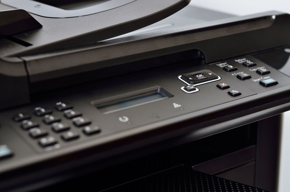 Close-up of a black multifunction printer control panel, featuring a keypad, display screen, and various buttons for copying and scanning functions.